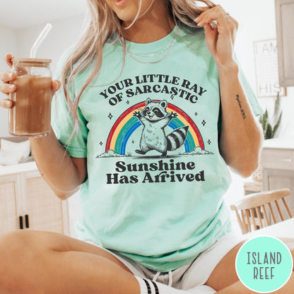 Comfort Colors tee in Island Reef featuring vintage style graphic of a happy raccoon standing before a colorful rainbow