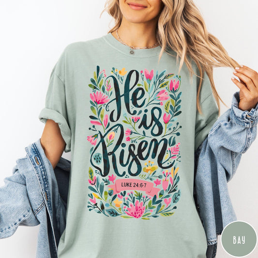 Comfort Colors tee in Bay featuring Easter religious floral graphic with He is Risen and Luke 24:6-7 text
