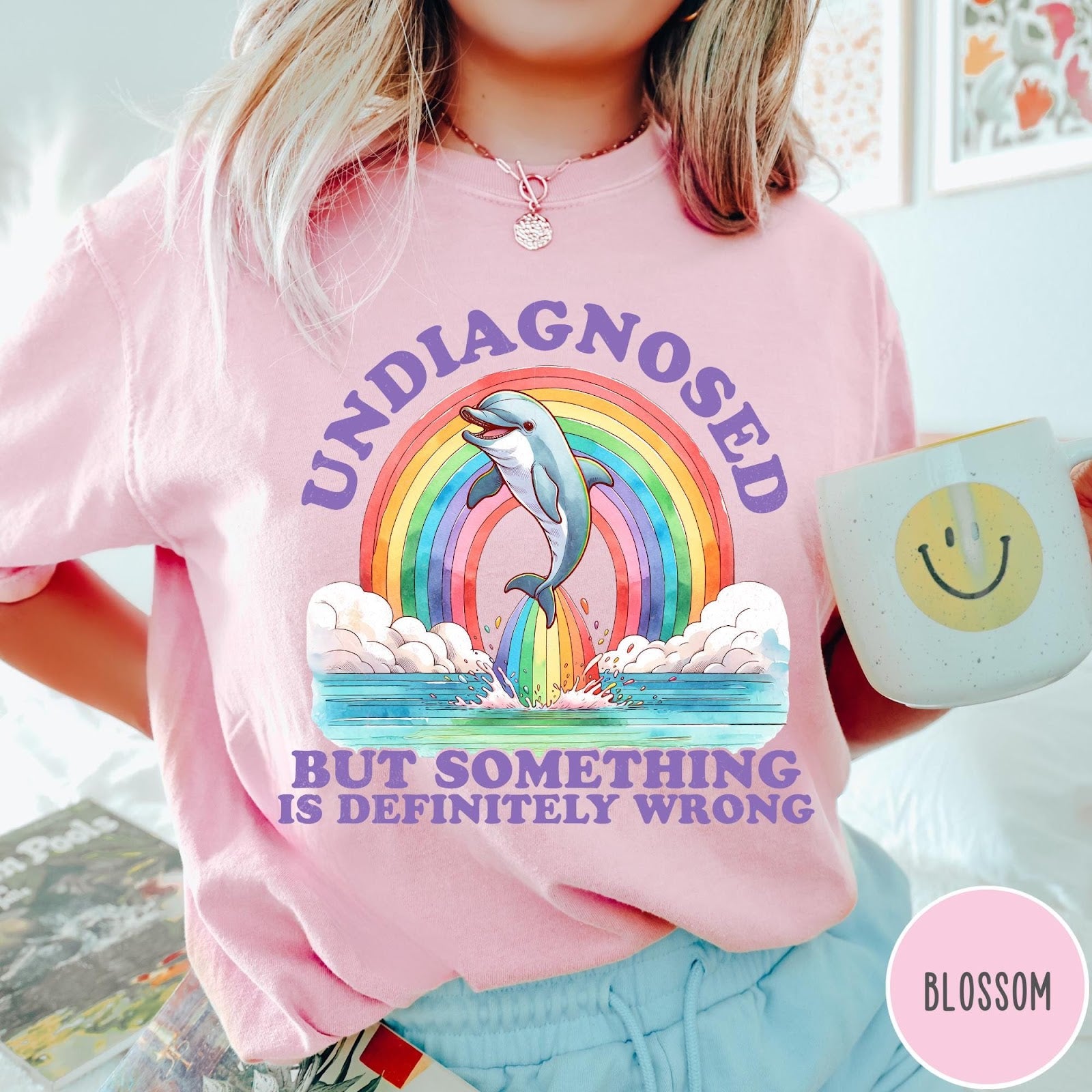 Comfort Colors tee in Blossom featuring graphic style illustration of a dolphin jumping through a colorful rainbow