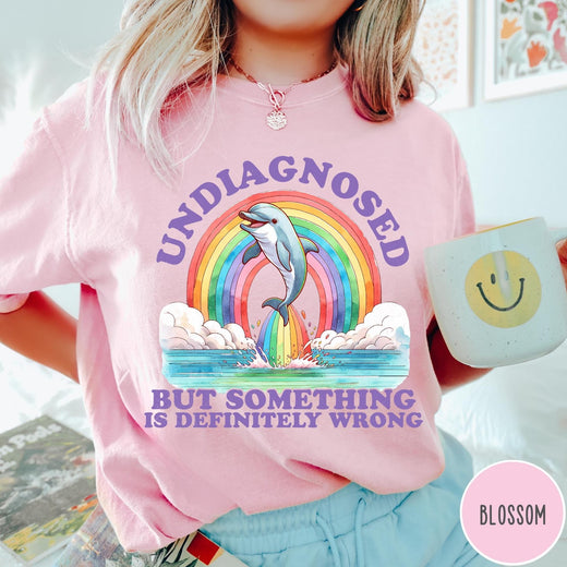Comfort Colors tee in Blossom featuring graphic style illustration of a dolphin jumping through a colorful rainbow