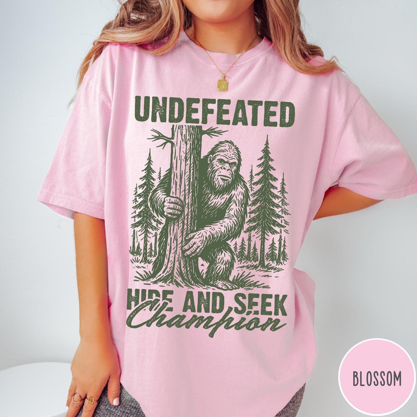 Comfort Colors tee in Blossom featuring vintage style graphic of Bigfoot hiding behind a large pine tree