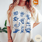 Comfort Colors tee in Ivory featuring whimsical space design with multiple raccoons wearing glass astronaut helmets and stars