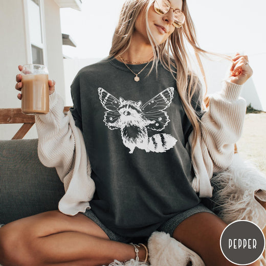 Comfort Colors tee in Pepper featuring whimsical graphic style of a raccoon with large detailed butterfly wings