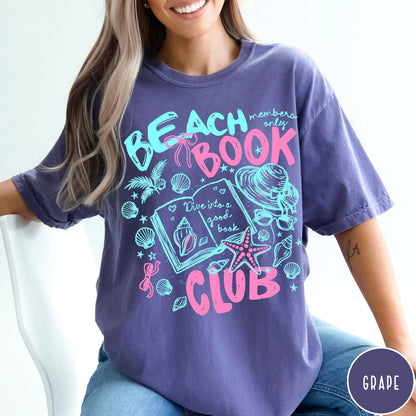 Comfort Colors tee in Grape featuring beach book club graphic with seashells, starfish, and a sun hat