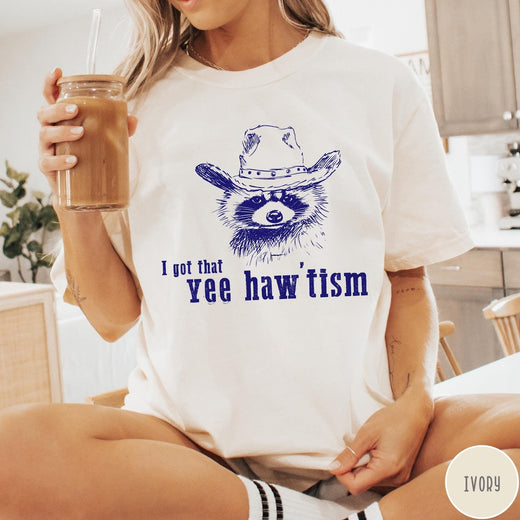 Comfort Colors tee in Ivory featuring western style graphic of a raccoon wearing a cowboy hat