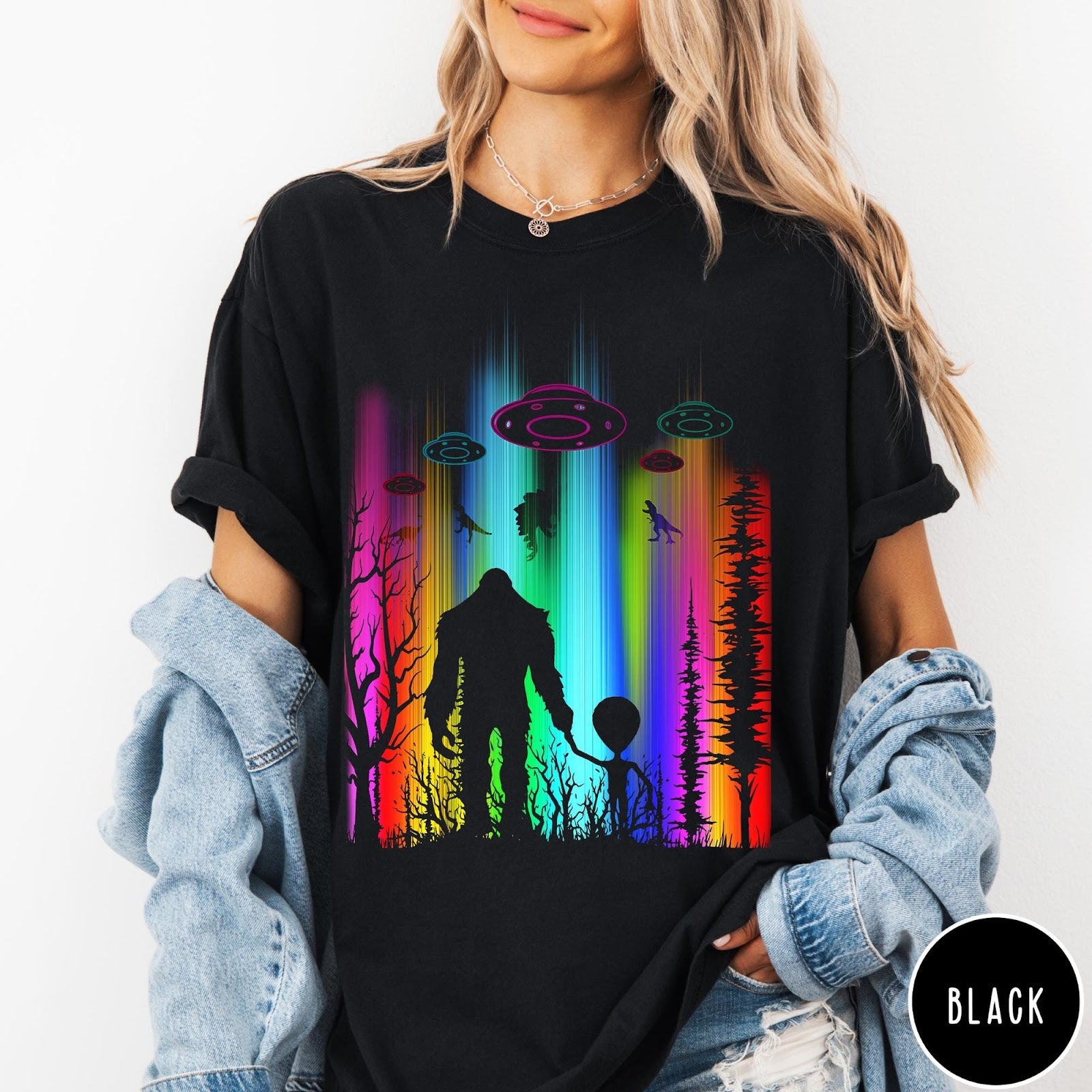 Comfort Colors tee in Black featuring a vibrant graphic of Bigfoot and an alien holding hands in forest