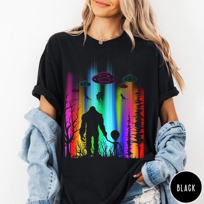 Comfort Colors tee in Black featuring a vibrant graphic of Bigfoot and an alien holding hands in forest
