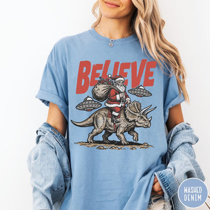 Comfort Colors tee in Washed Denim featuring graphic illustration of Santa riding a dinosaur with flying saucers above