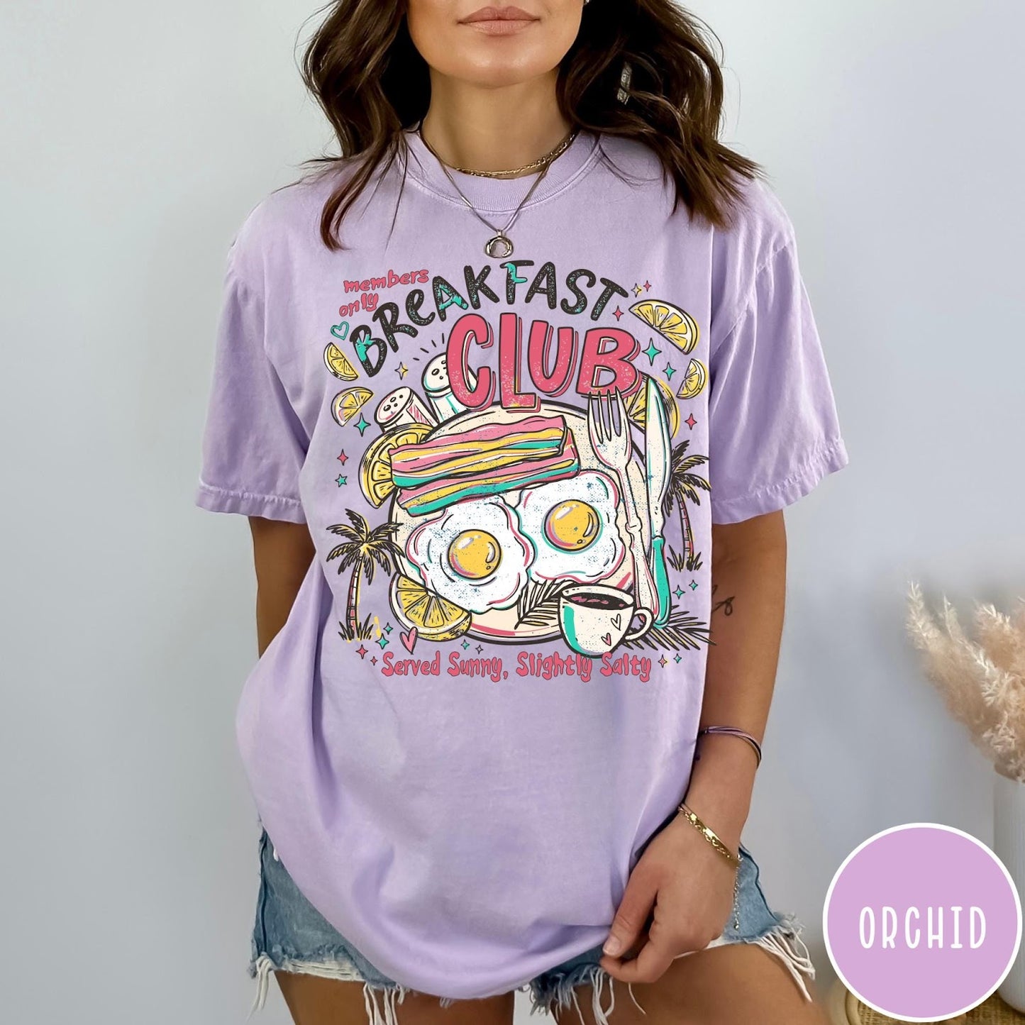 Comfort Colors tee in Orchid featuring breakfast food graphic with bacon, eggs, coffee, and palm trees.