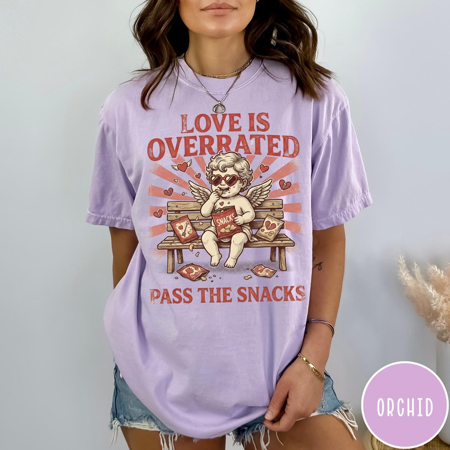 Comfort Colors tee in Orchid featuring vintage style graphic of a cherub eating snacks on a bench