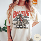 Comfort Colors tee in Ivory featuring vintage style graphic of Santa riding a dinosaur with flying saucers