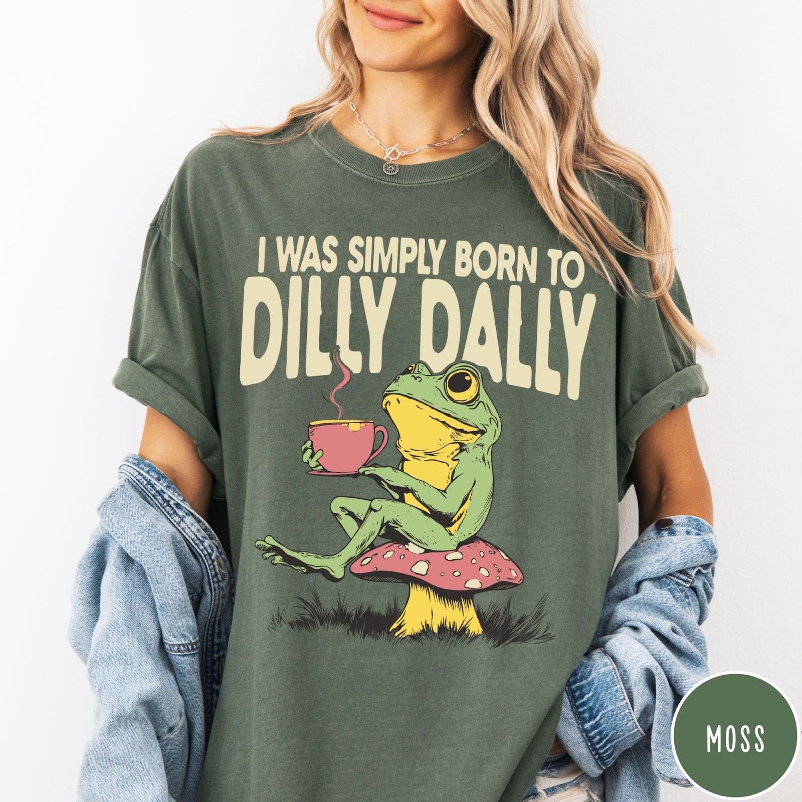 Comfort Colors tee in Moss featuring illustrative style graphic of a frog sitting on a mushroom drinking tea