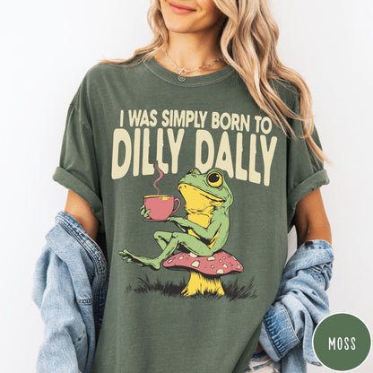 Comfort Colors tee in Moss featuring illustrative style graphic of a frog sitting on a mushroom drinking tea