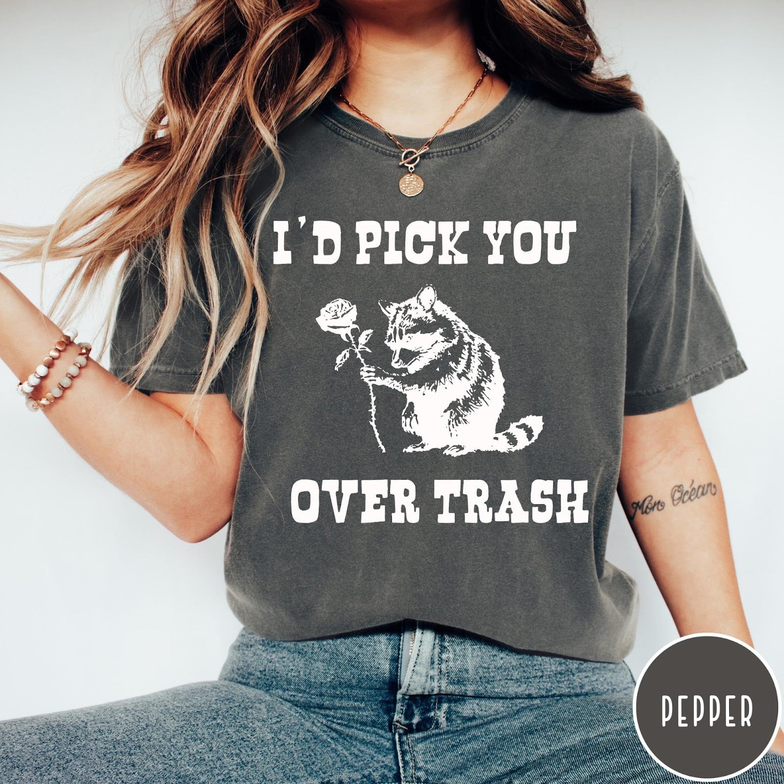 Comfort Colors tee in Pepper featuring a whimsical graphic of a raccoon holding a white rose.