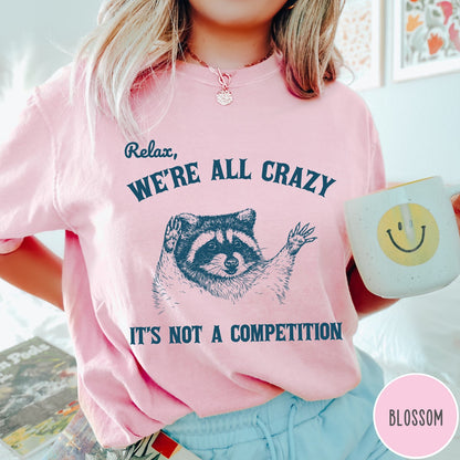Comfort Colors tee in Blossom featuring screen print style graphic of a raccoon with text Relax We Are All Crazy