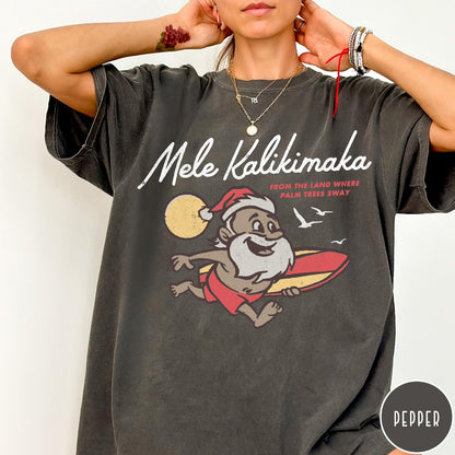 Comfort Colors tee in Pepper featuring vintage style graphic of a surfing Santa Claus on vacation