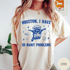 Comfort Colors tee in Ivory featuring space style graphic of a raccoon wearing an astronaut helmet floating