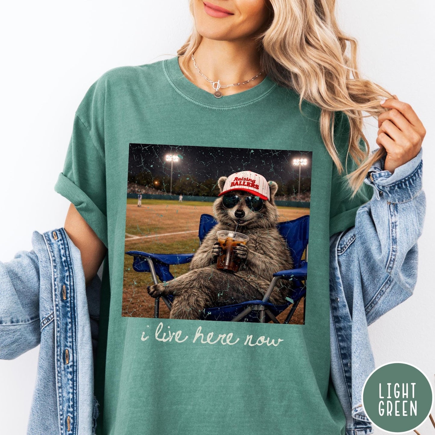 Comfort Colors tee in Light Green featuring graphic raccoon wearing sunglasses and baseball cap sitting in camping chair