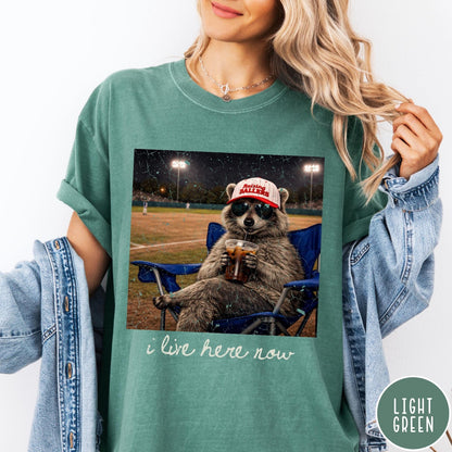 Comfort Colors tee in Light Green featuring graphic raccoon wearing sunglasses and baseball cap sitting in camping chair