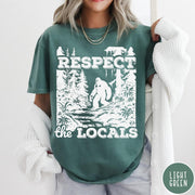 Comfort Colors tee in Light Green featuring vintage style graphic of Bigfoot walking through a forest by a river