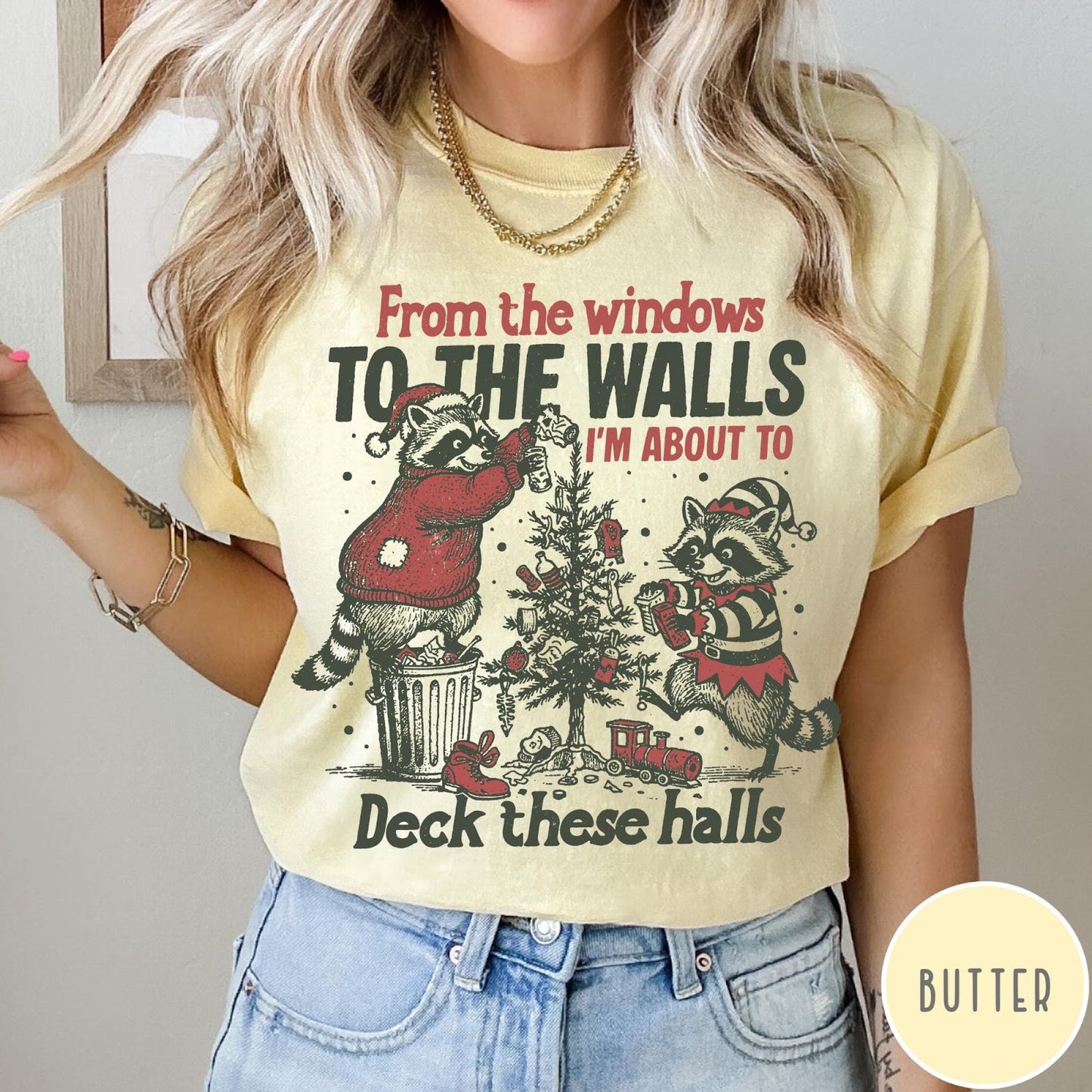 Comfort Colors tee in Butter featuring festive graphic of two raccoons decorating a Christmas tree with holiday text