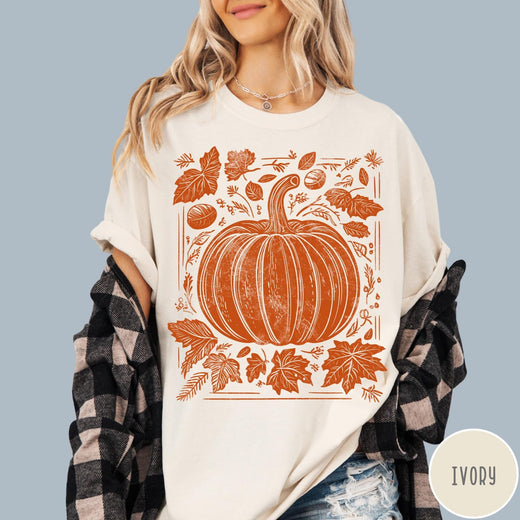 Comfort Colors tee in Ivory featuring rustic pumpkin design with surrounding fall leaves and woodland elements