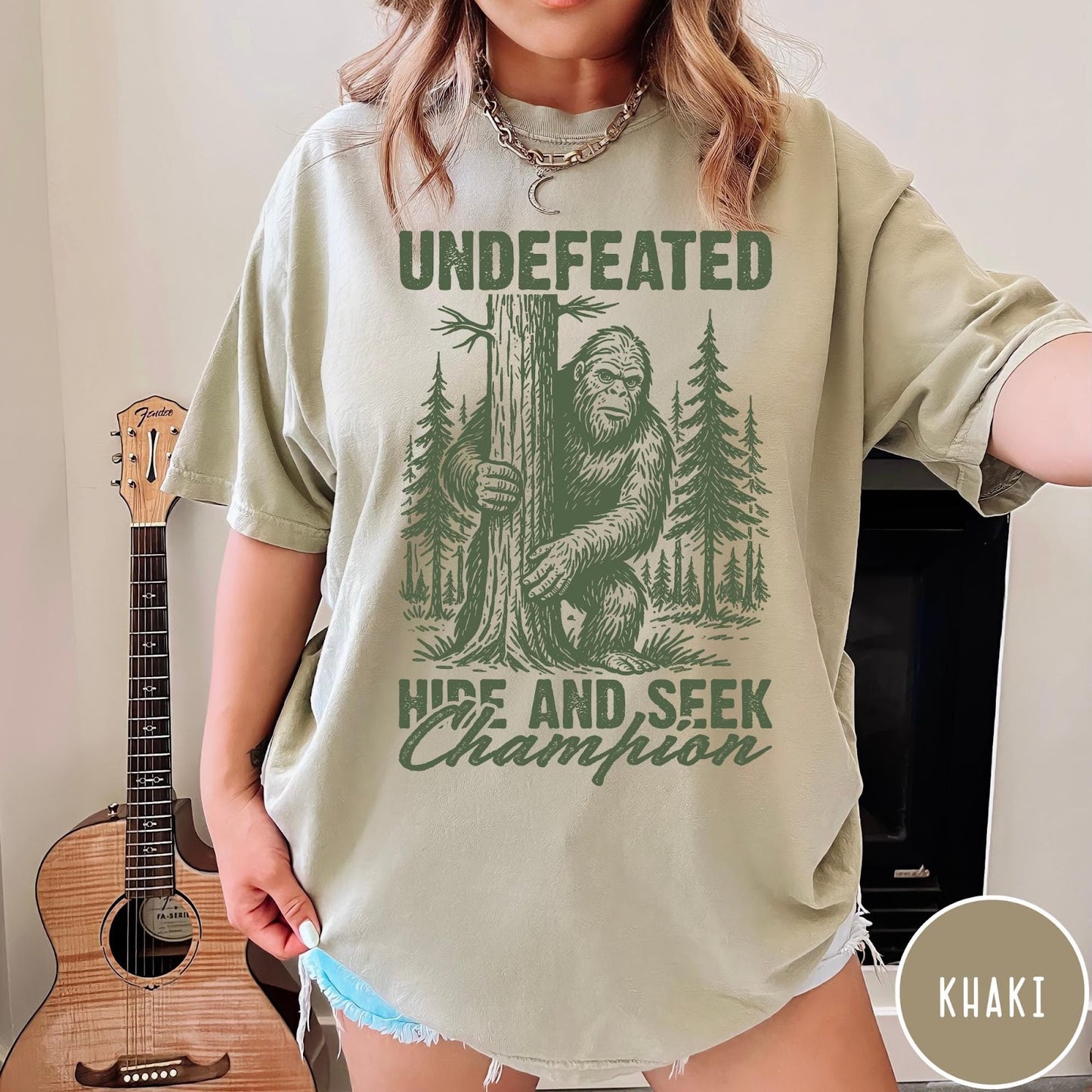Comfort Colors tee in Khaki featuring vintage style Bigfoot graphic hiding behind a tree in the forest