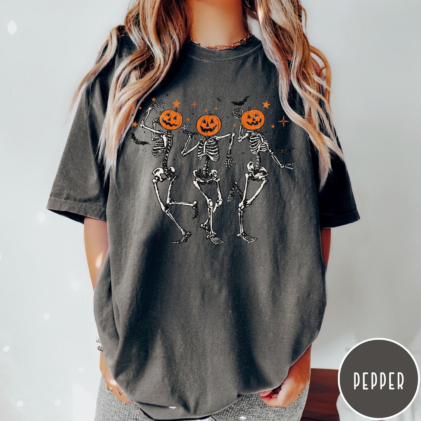 Comfort Colors tee in Pepper featuring dancing skeleton graphic with jack-o'-lantern heads and small orange stars