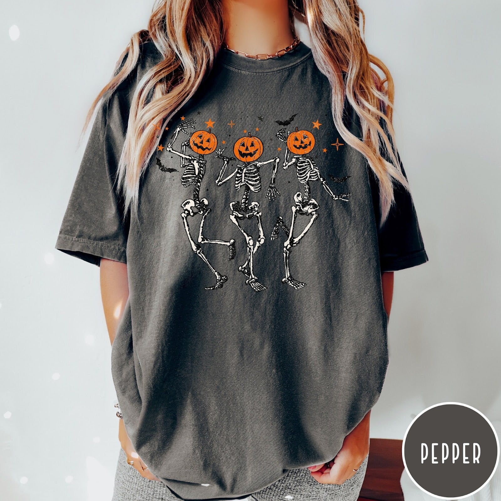 Comfort Colors tee in Pepper featuring dancing skeleton graphic with jack-o'-lantern heads and small orange stars