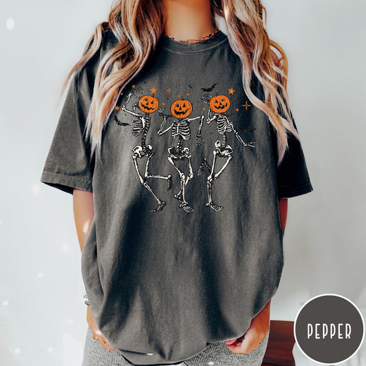 Comfort Colors tee in Pepper featuring dancing skeleton graphic with jack-o'-lantern heads and small orange stars
