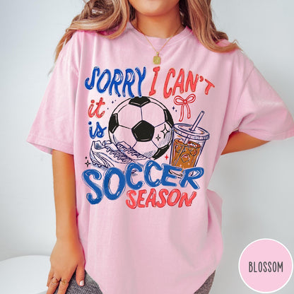 Comfort Colors tee in Blossom featuring soccer season graphic with soccer ball, cleats, and iced coffee