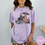 Comfort Colors tee in Orchid featuring western style graphic of a cowboy on horseback under a UFO