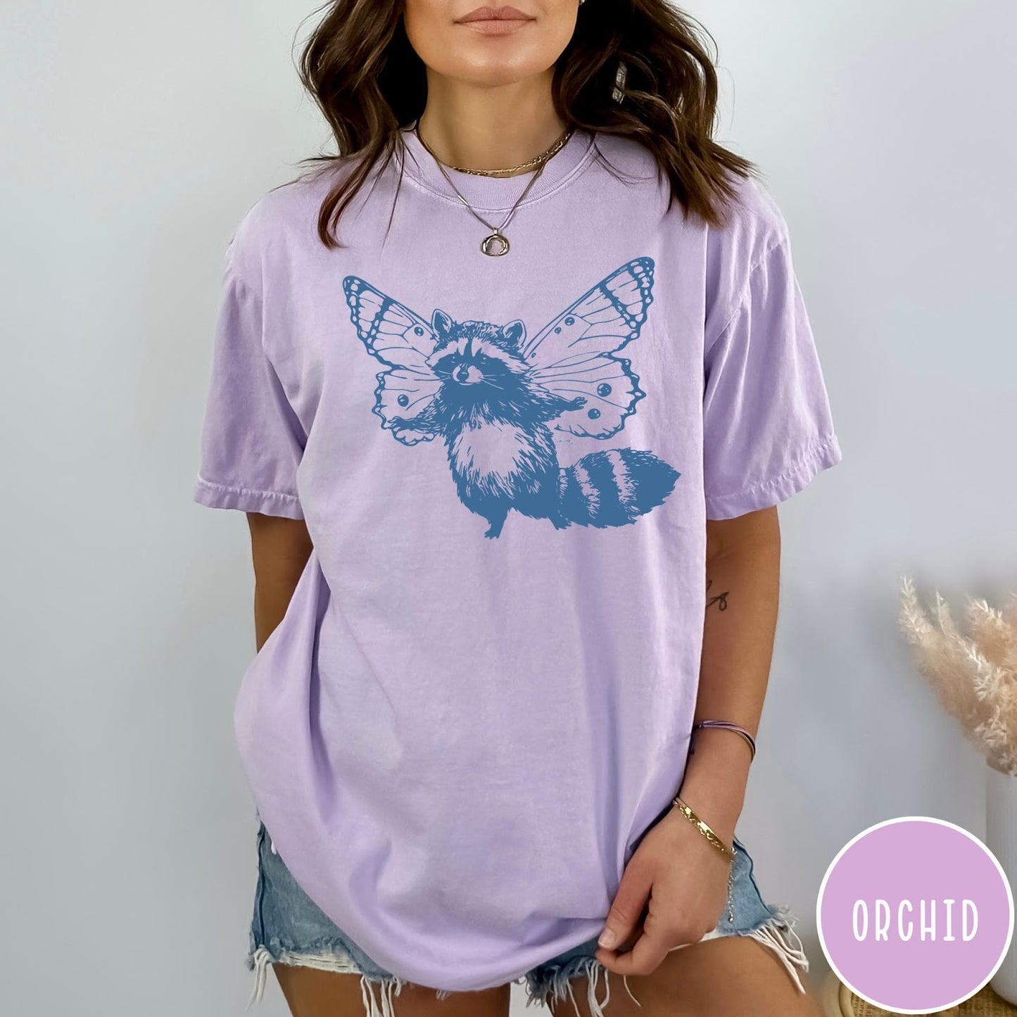 Comfort Colors tee in Orchid featuring whimsical graphic style of a raccoon with large detailed butterfly wings