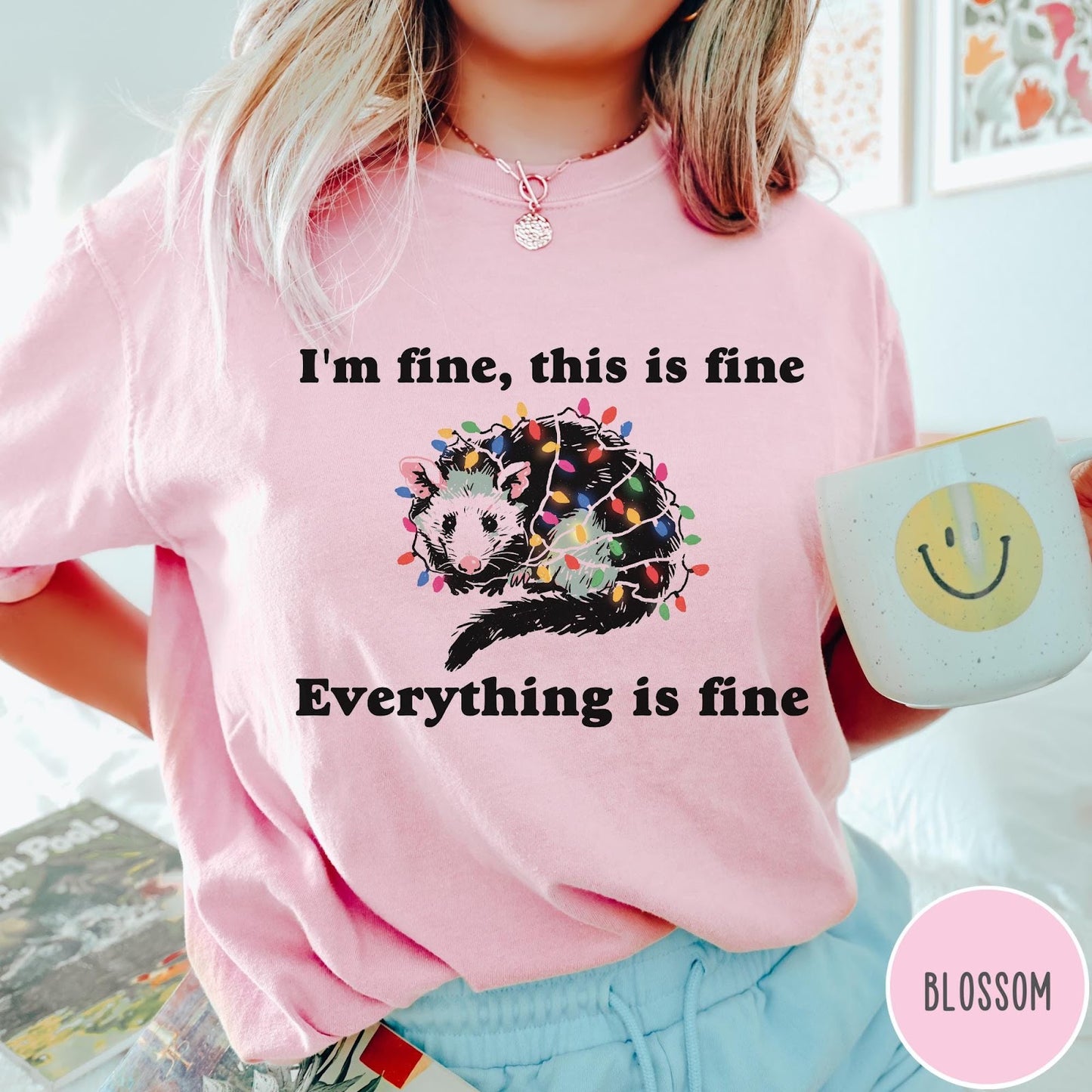 Comfort Colors tee in Blossom featuring graphic illustration of an opossum tangled in colorful Christmas lights