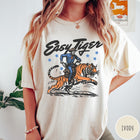 Comfort Colors tee in Ivory featuring western graphic style cowboy riding a tiger with blue stars