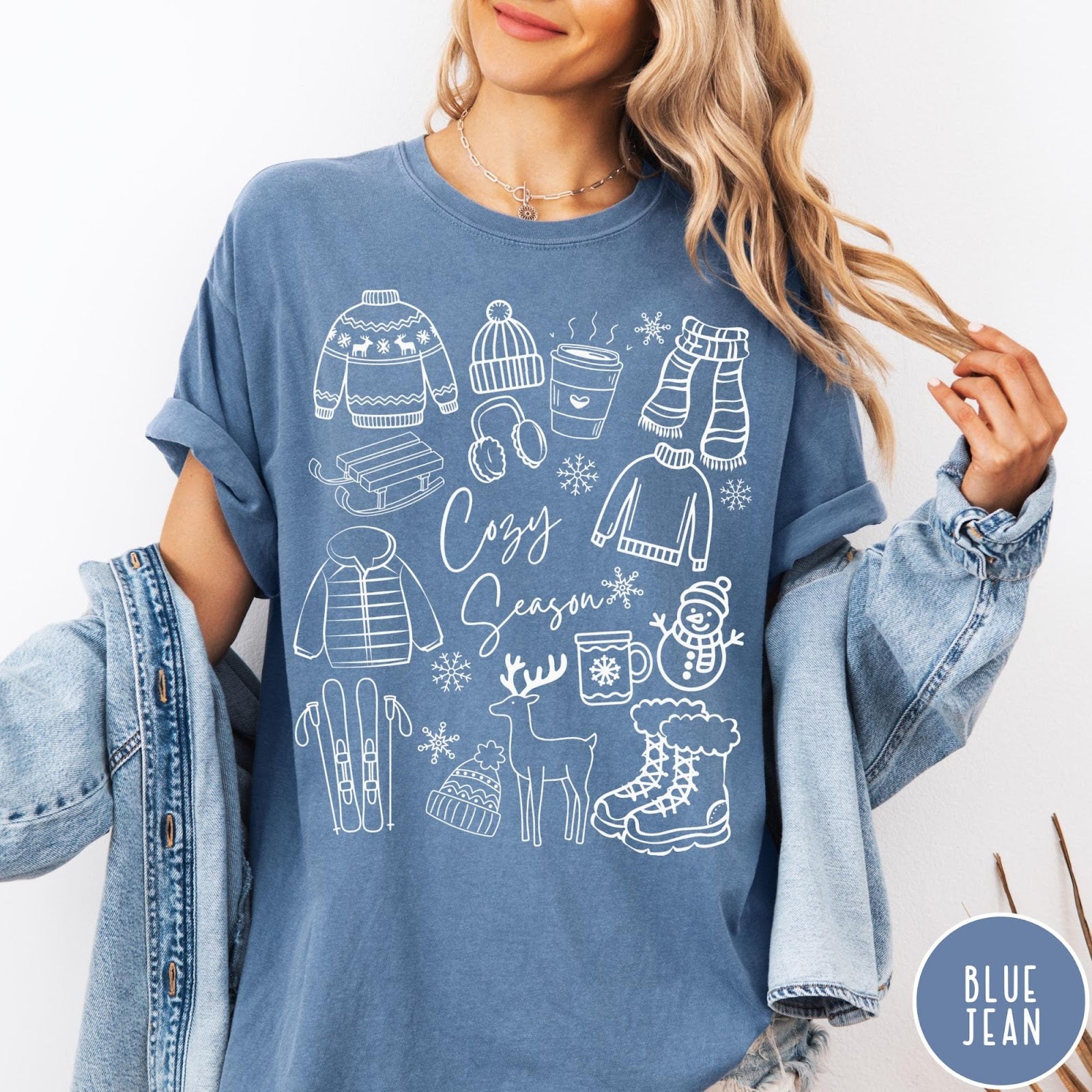 Comfort Colors tee in Blue Jean featuring winter activities graphic with sweaters, sled, snowman, and seasonal items.