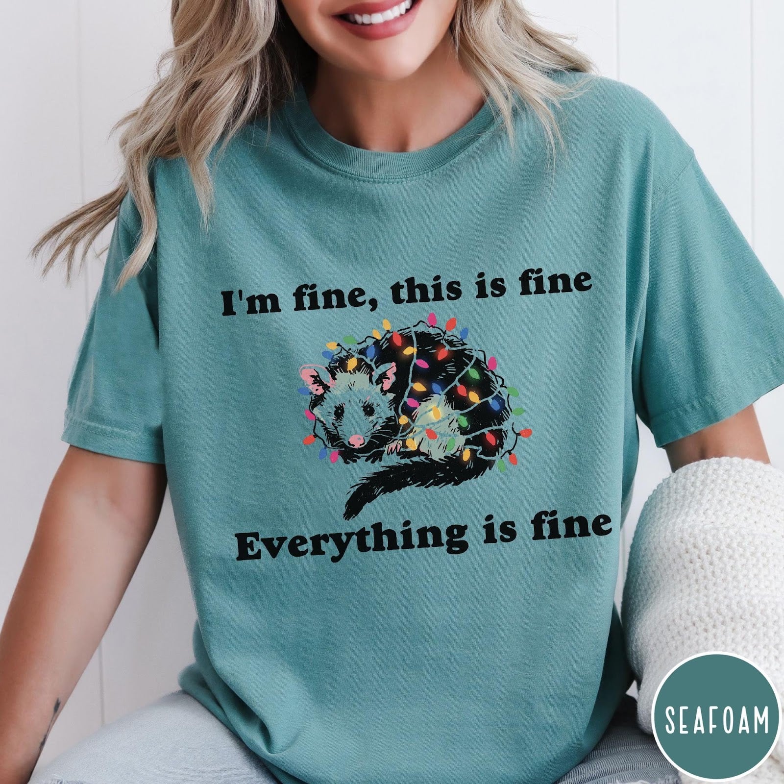 Comfort Colors tee in Seafoam featuring graphic illustration of an opossum tangled in colorful Christmas lights