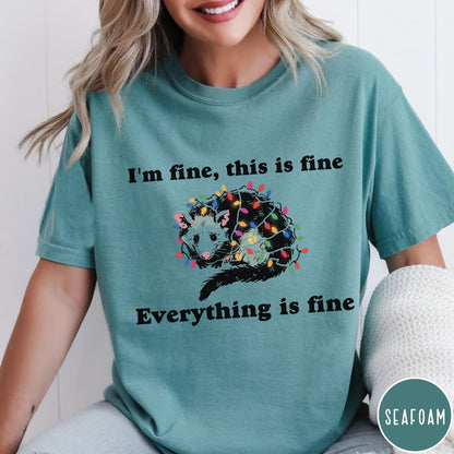 Comfort Colors tee in Seafoam featuring graphic illustration of an opossum tangled in colorful Christmas lights
