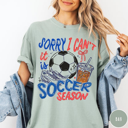 Comfort Colors tee in Bay featuring soccer season graphic with soccer ball, cleats, and iced coffee
