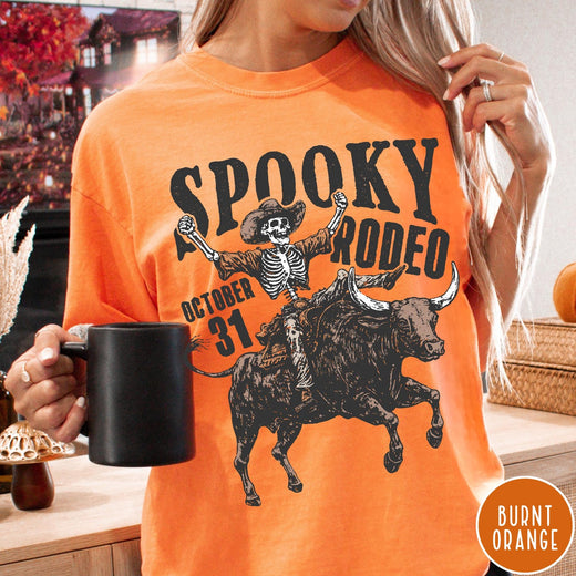 Comfort Colors tee in Burnt Orange featuring western style graphic of a skeleton cowboy riding a bucking bull