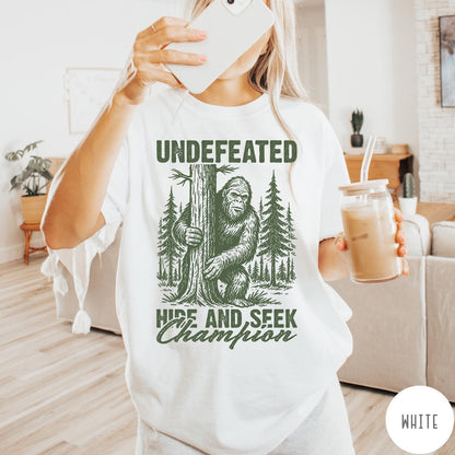 Comfort Colors tee in White featuring vintage style Bigfoot graphic hiding behind a tree in the forest