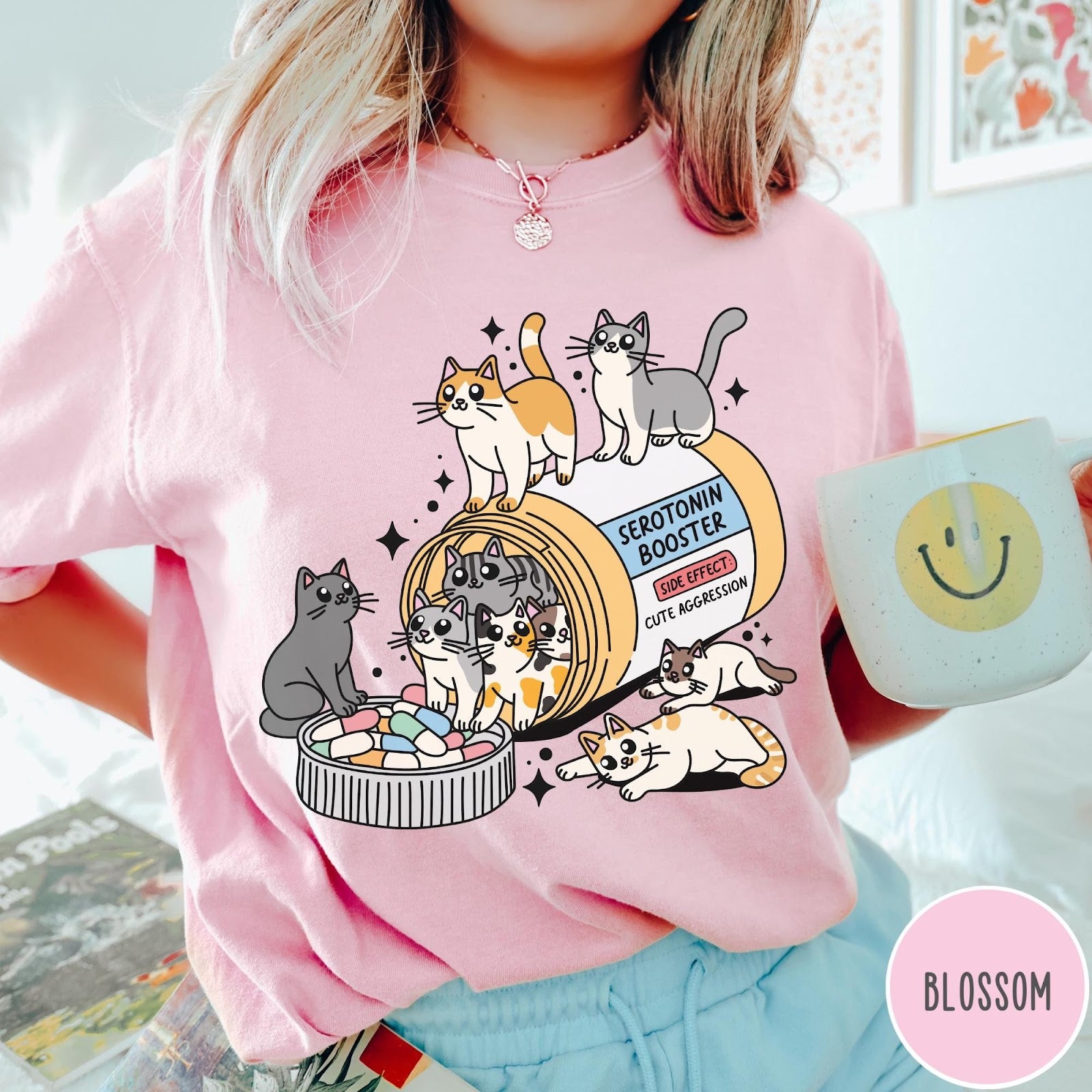 Comfort Colors tee in Blossom featuring graphic illustration of cats spilling out of a serotonin booster bottle