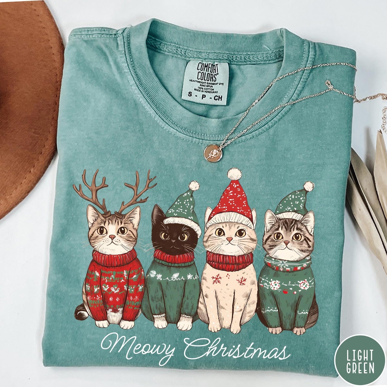 Comfort Colors tee in Light Green featuring holiday graphic of four cats wearing Christmas sweaters and hats