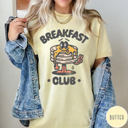 Comfort Colors tee in Butter featuring retro style graphic of a pancake character with syrup and peace sign