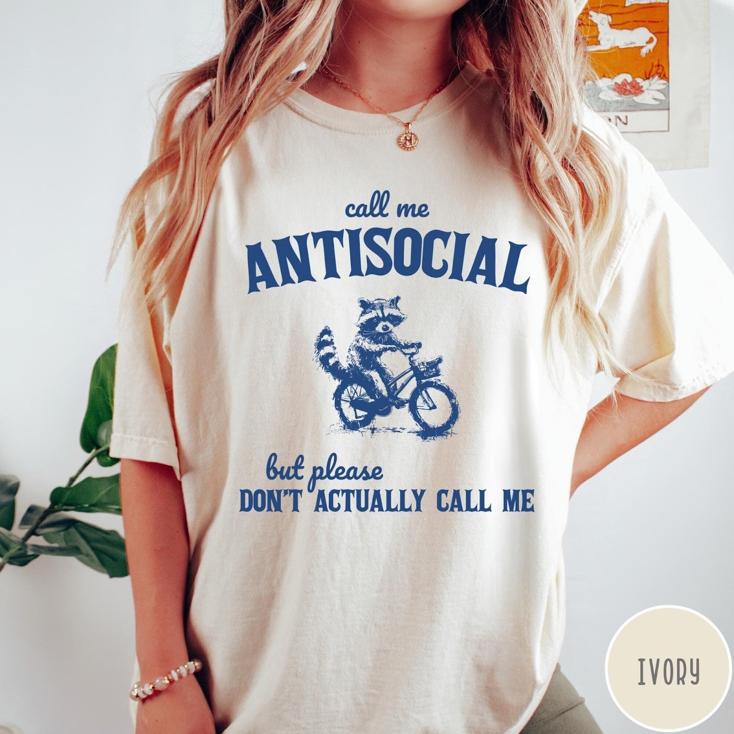 Comfort Colors tee in Ivory featuring graphic style illustration of a raccoon riding a bicycle