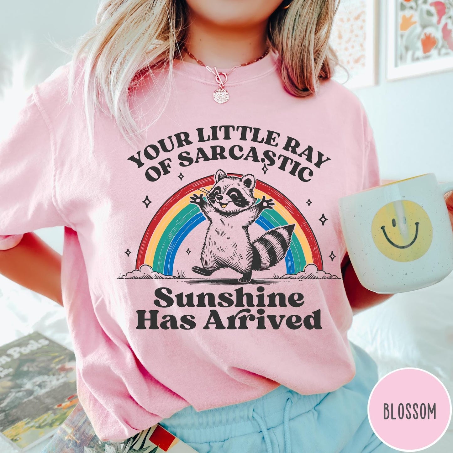 Comfort Colors tee in Blossom featuring vintage style graphic of a happy raccoon standing before a colorful rainbow