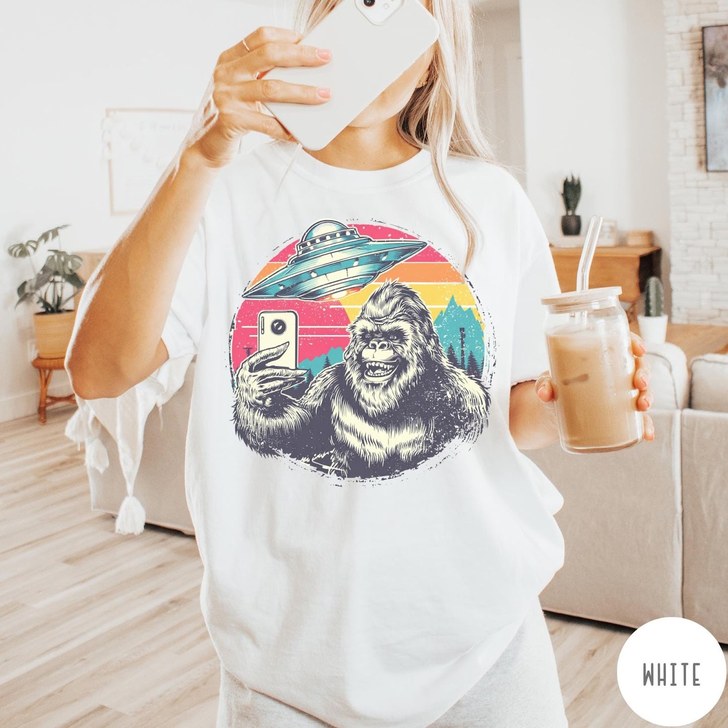Comfort Colors tee in White featuring retro Bigfoot selfie graphic with a UFO and sunset mountain background