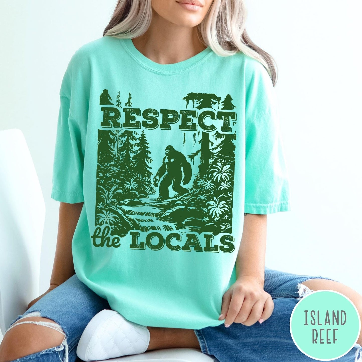 Comfort Colors tee in Island Reef featuring vintage style graphic of Bigfoot walking through a forest by a river