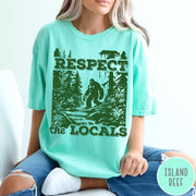 Comfort Colors tee in Island Reef featuring vintage style graphic of Bigfoot walking through a forest by a river