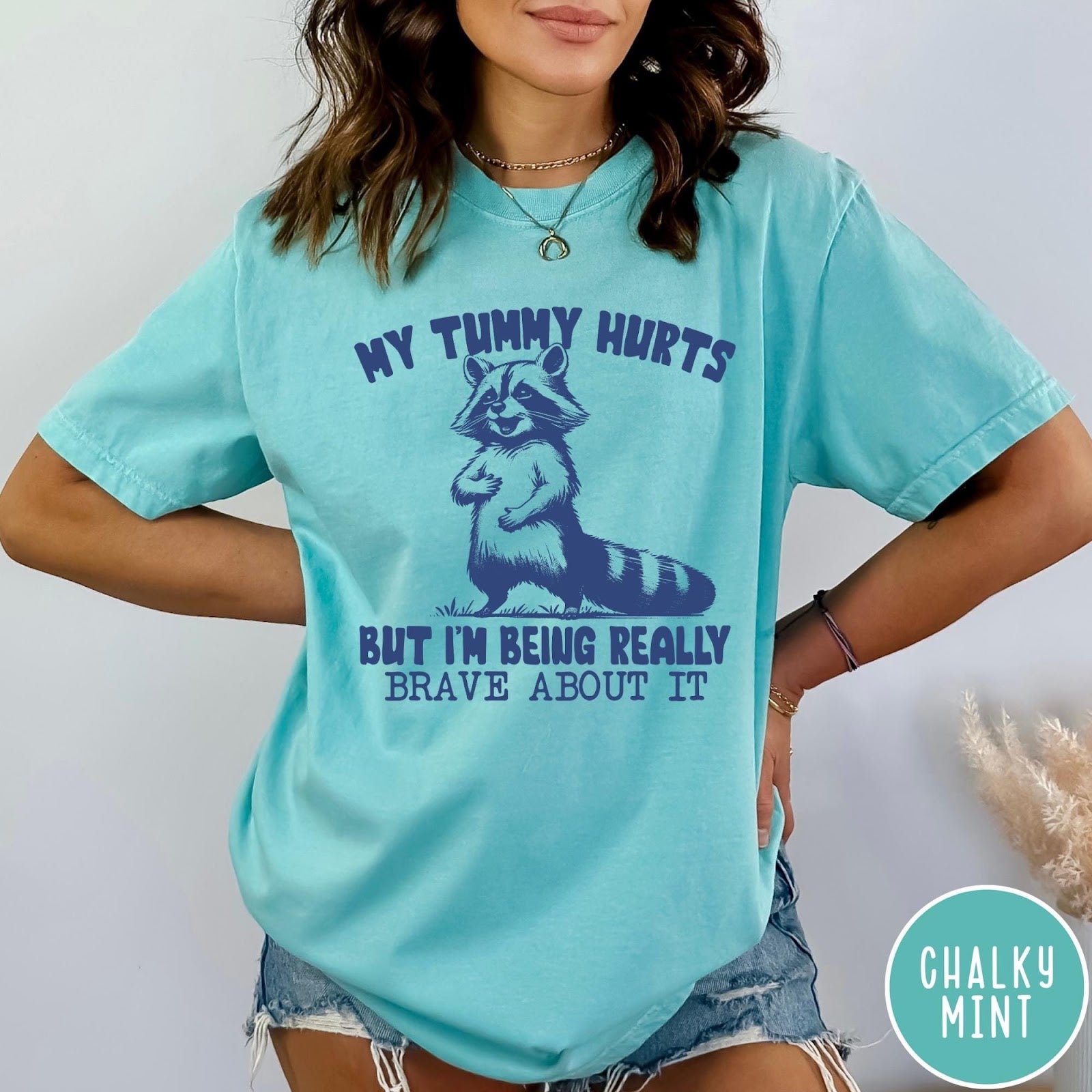 Comfort Colors tee in Chalky Mint featuring graphic illustration of a standing raccoon with funny text about being brave